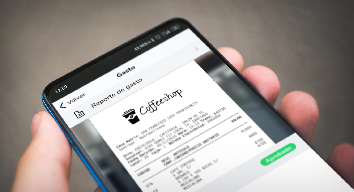 APP_movilPrimer plano de una mano sosteniendo un smartphone que muestra la pantalla de la aplicación de Rindegastos. En la pantalla se ve un reporte de gasto que incluye una imagen digitalizada de un recibo de un lugar llamado "Coffeeshop." En la parte inferior derecha de la pantalla, hay un botón verde con la palabra "Aprobado," indicando que el gasto ha sido revisado y aprobado.