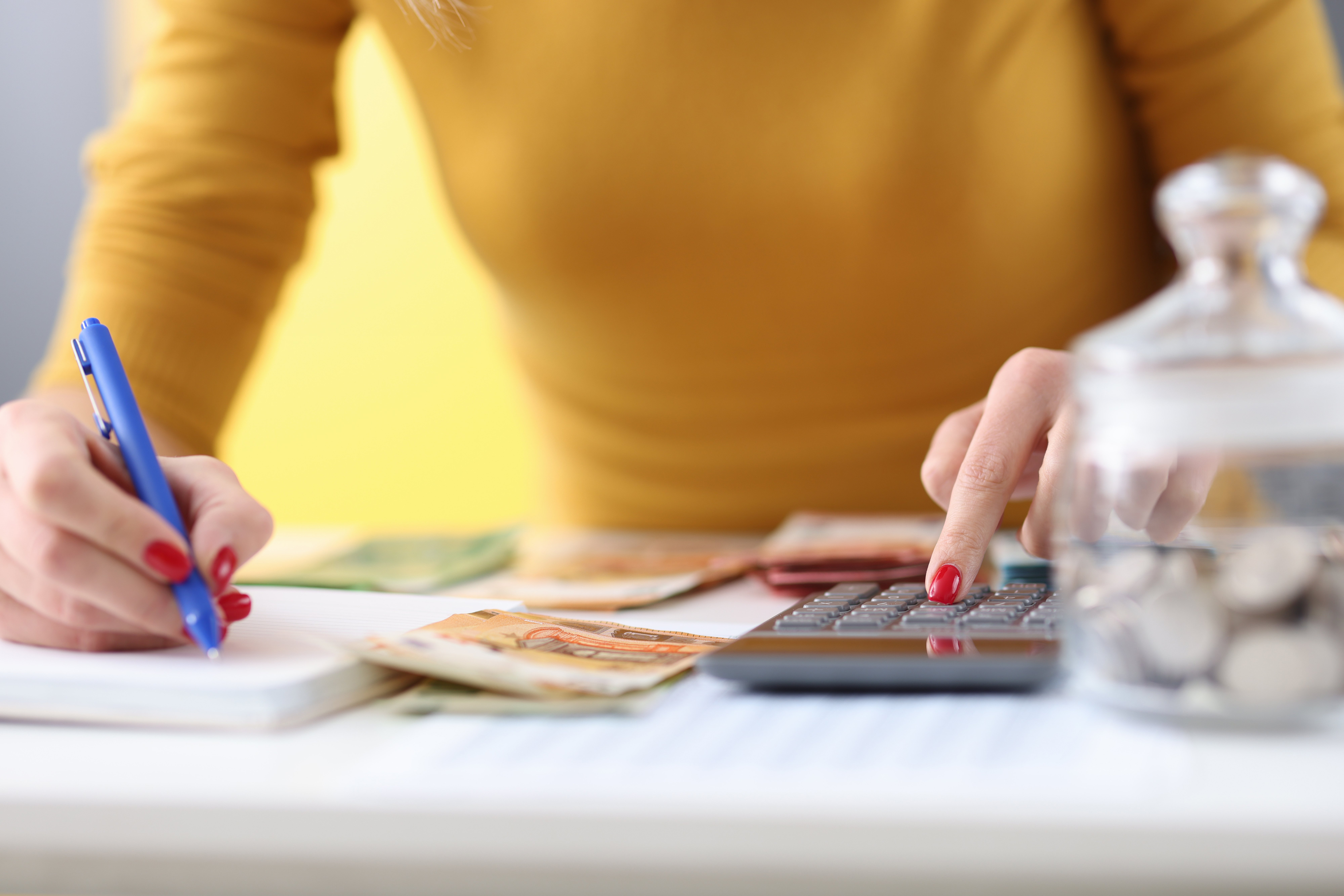 Persona escribiendo en una libreta y usando una calculadora, con billetes y monedas sobre la mesa, representando planificación financiera y control de gastos