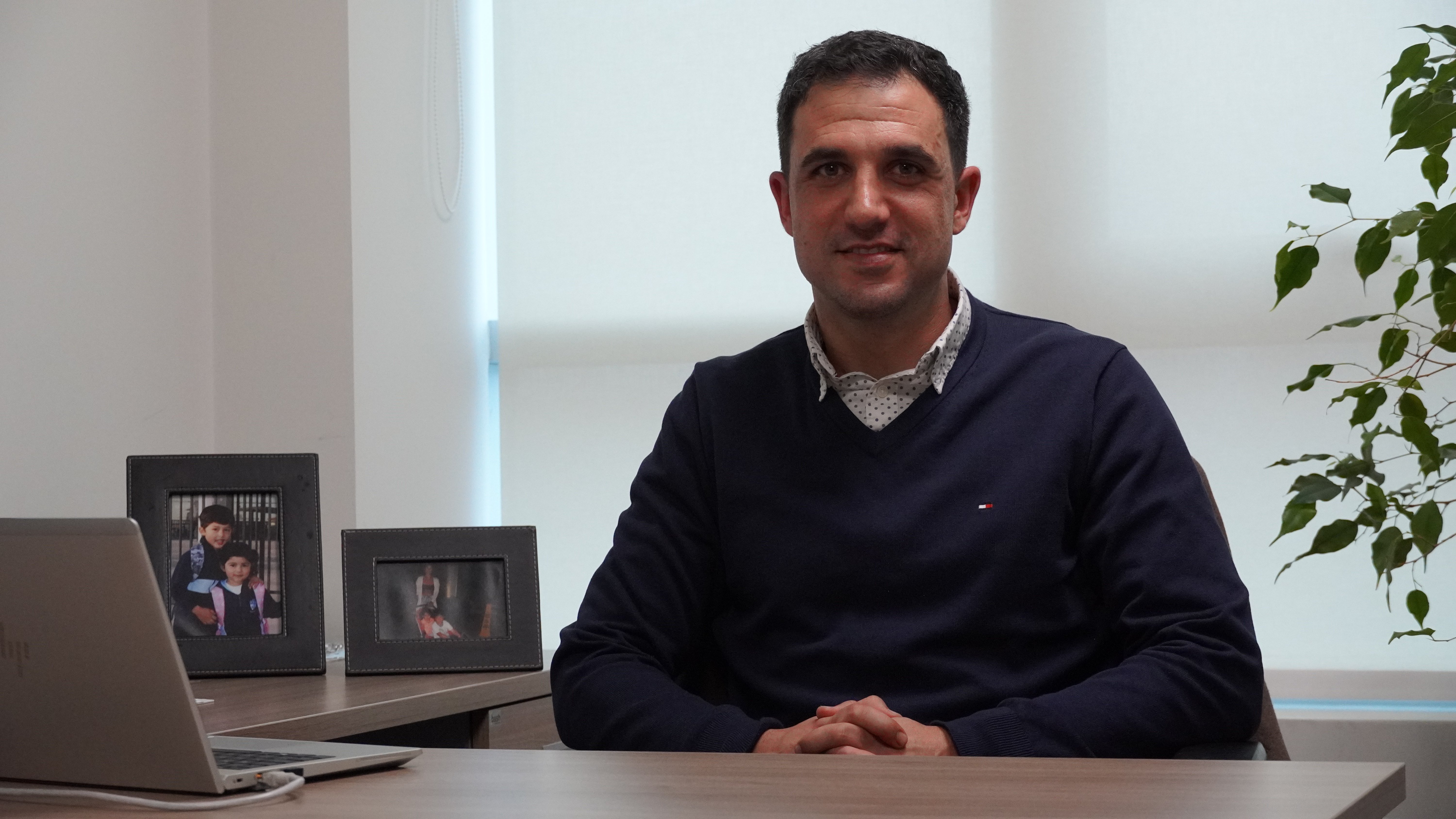 Retrato de un profesional sentado en su oficina, con una laptop y fotos familiares en el escritorio, simbolizando liderazgo empresarial.