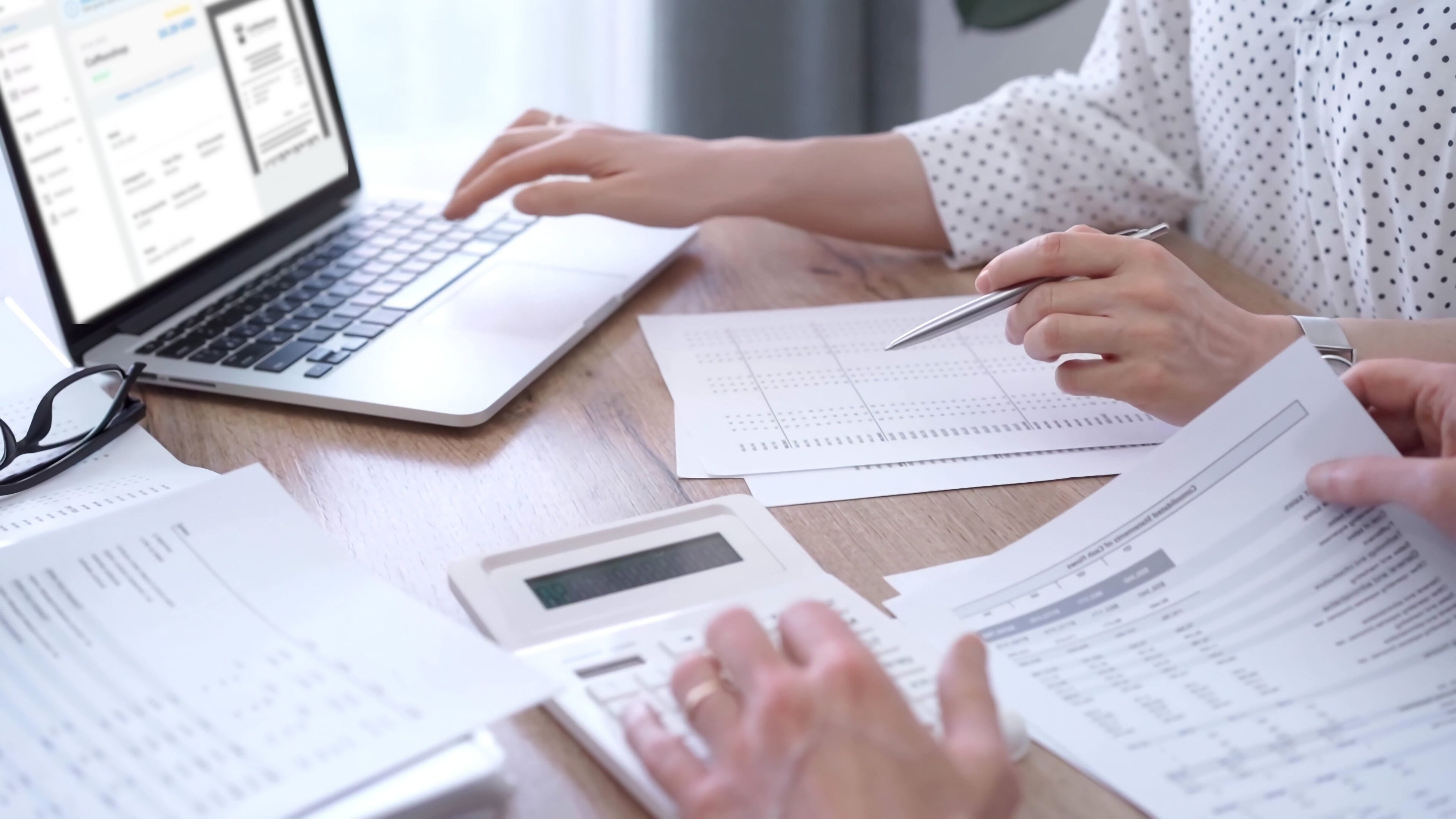 Dos personas revisando documentos y trabajando con una calculadora mientras usan una laptop que muestra Rindegastos