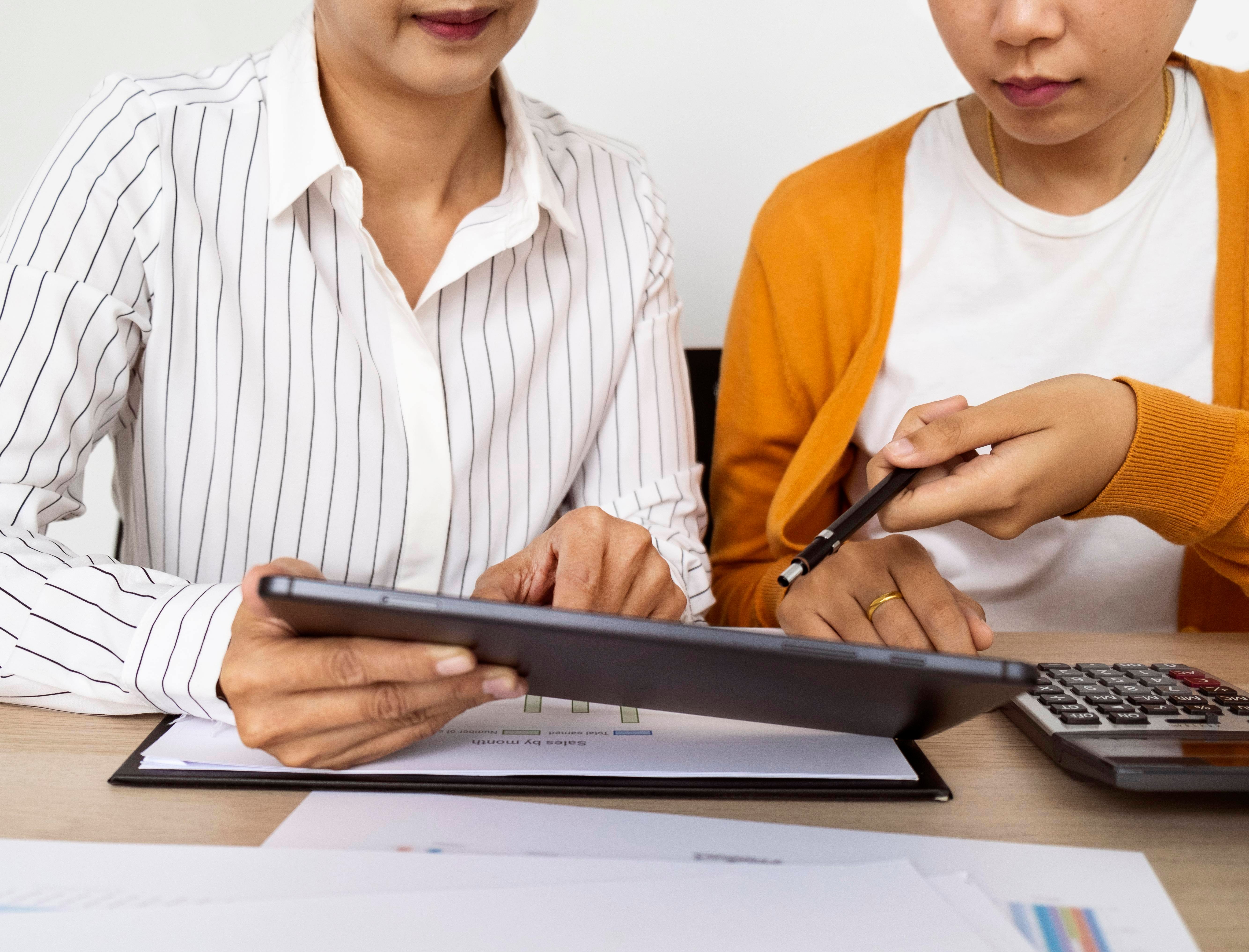 Dos personas trabajando en equipo mientras revisan información en una tableta, posiblemente analizando reportes financieros o datos de gastos.