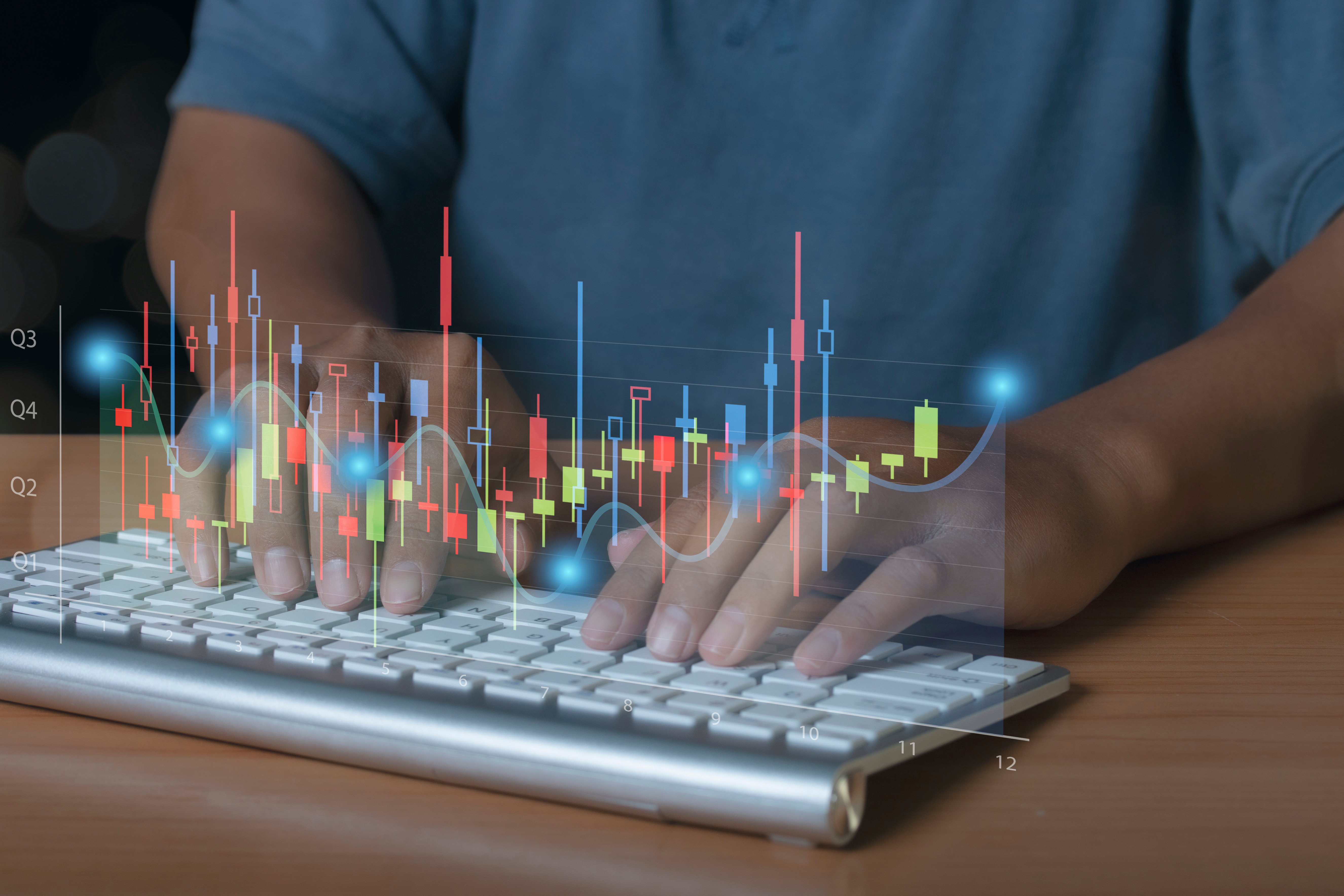 Manos de una persona escribiendo en un teclado, con gráficos financieros en superposición mostrando datos y tendencias.