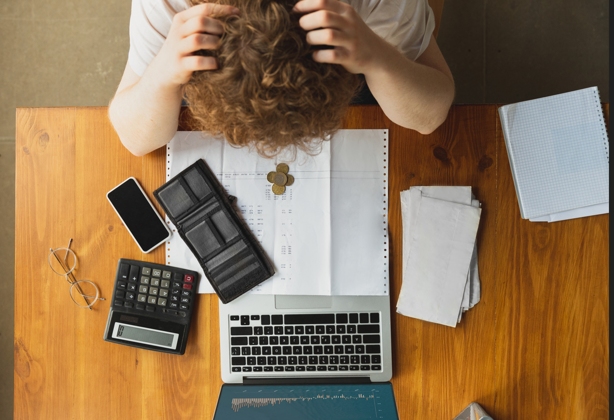 ersona revisando documentos financieros, con una calculadora, monedas y una laptop en el escritorio, simbolizando estrés