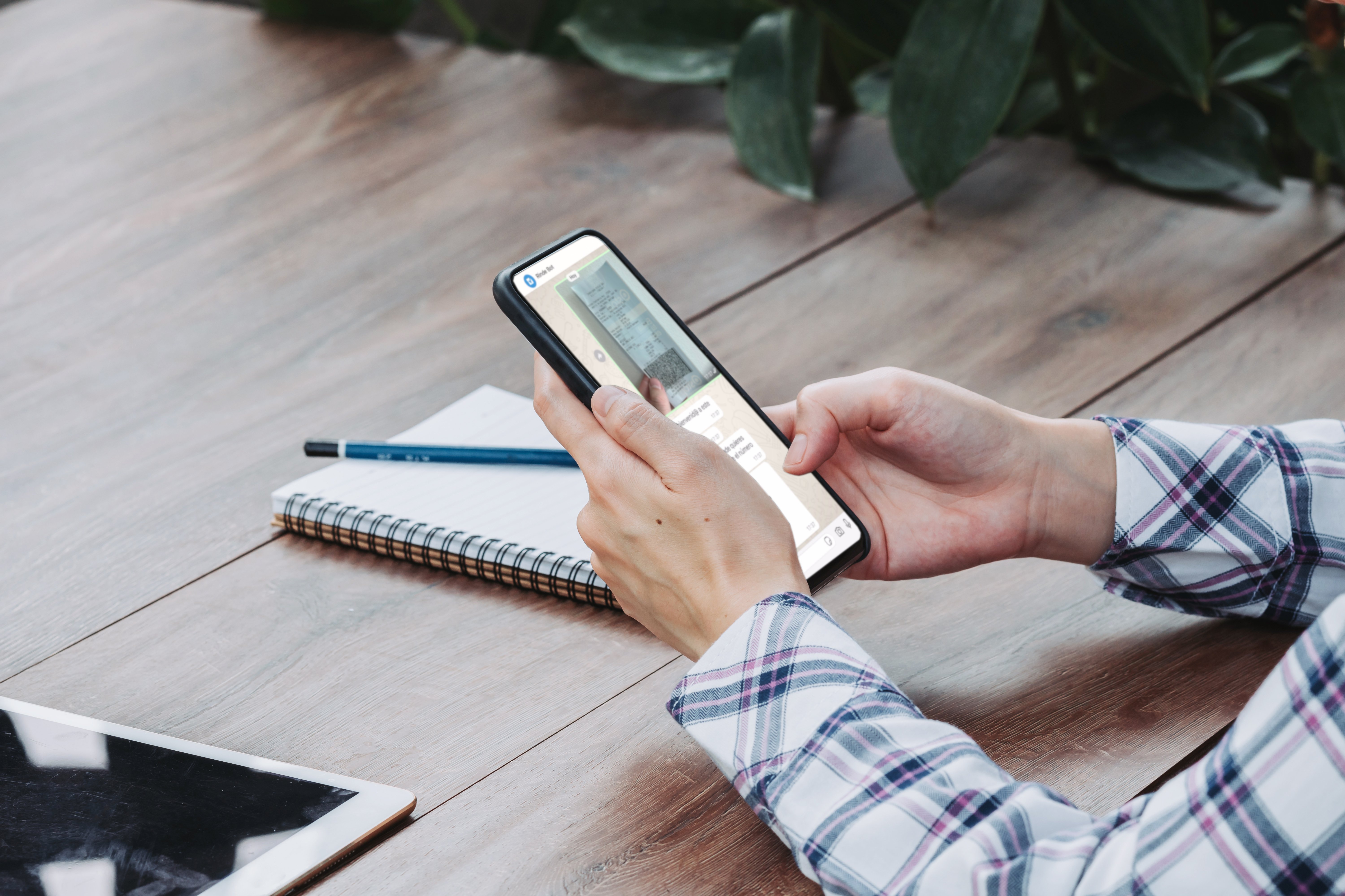 Persona sosteniendo un teléfono móvil con la aplicación de Rindegastos abierta, lista para registrar un gasto, con un cuaderno y una tablet sobre la mesa.