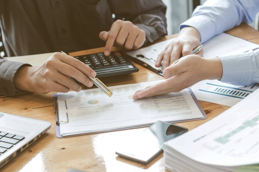 Dos personas revisando informes financieros con una calculadora y documentos en una mesa.