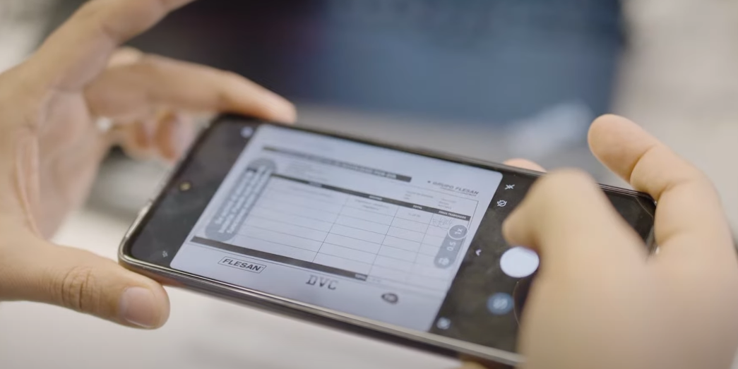 Manos de una persona utilizando un teléfono móvil con la APP de Rindegastos  para escanear un documento del Grupo Flesan, capturando los detalles del formulario.