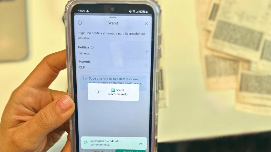 "Pantalla de smartphone mostrando la aplicación Rindegastos durante el proceso de sincronización de un recibo. La aplicación muestra opciones para elegir políticas y moneda para el gasto, con un mensaje indicando que la imagen ha sido editada correctamente y la sincronización está en progreso.