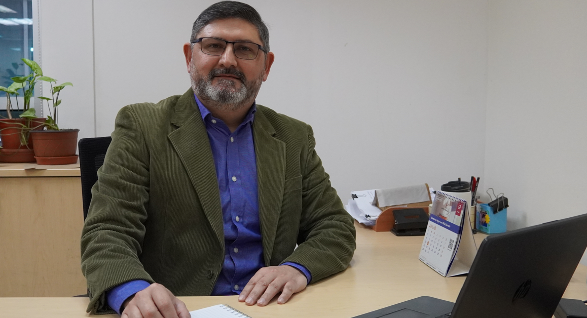 Retrato de un ejecutivo sentado en su oficina, con laptop y cuaderno en el escritorio, acompañado de plantas en macetas que añaden un toque natural al ambiente laboral.