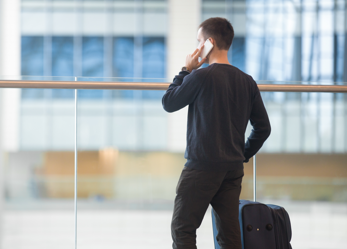 Hombre hablando por teléfono en el aeropuerto con maleta a su lado, representando un viaje de negocios.