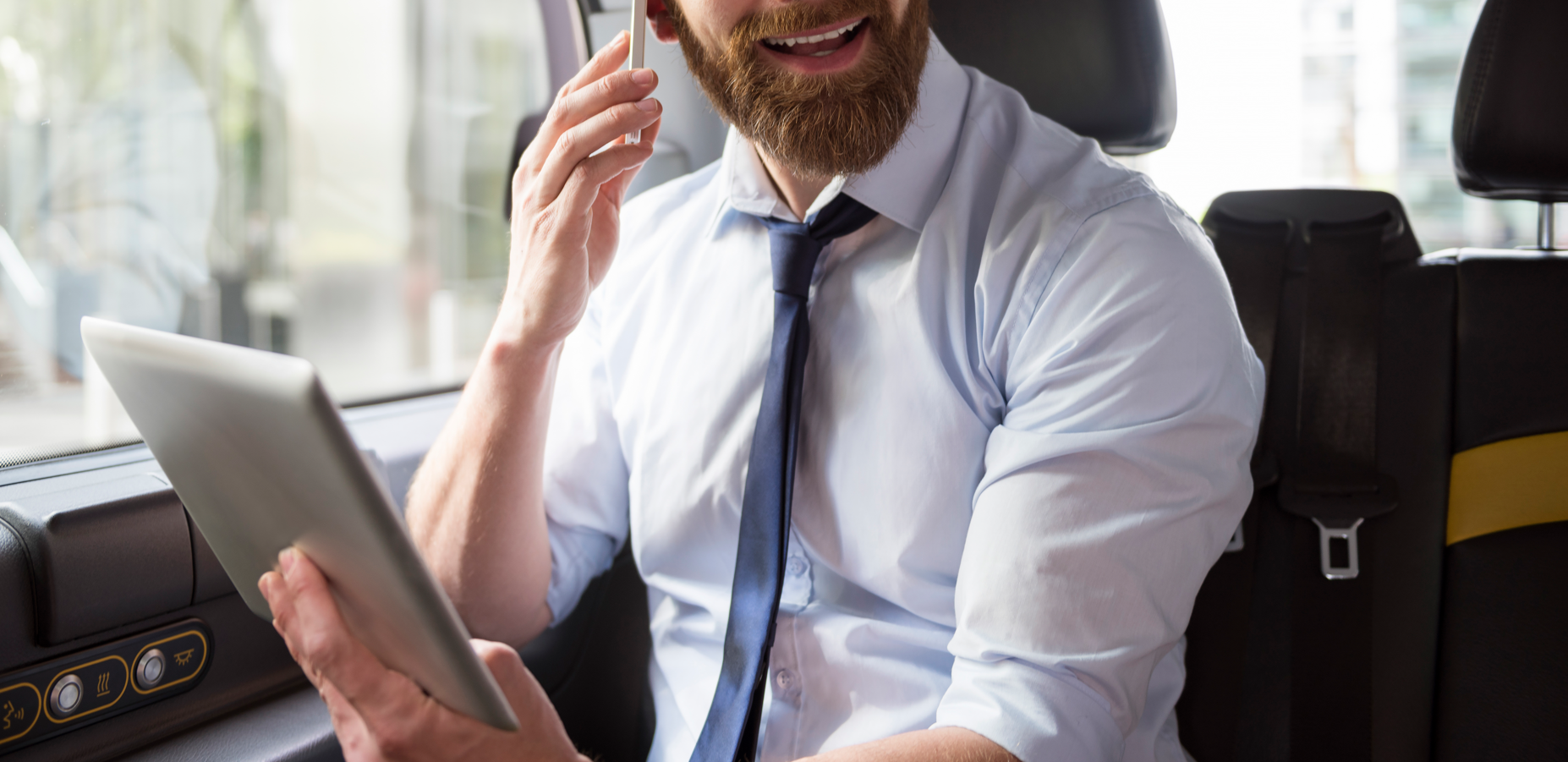 Ejecutivo hablando por teléfono y revisando documentos en tablet mientras viaja en auto. Soluciones para movilidad y trabajo remoto eficiente.