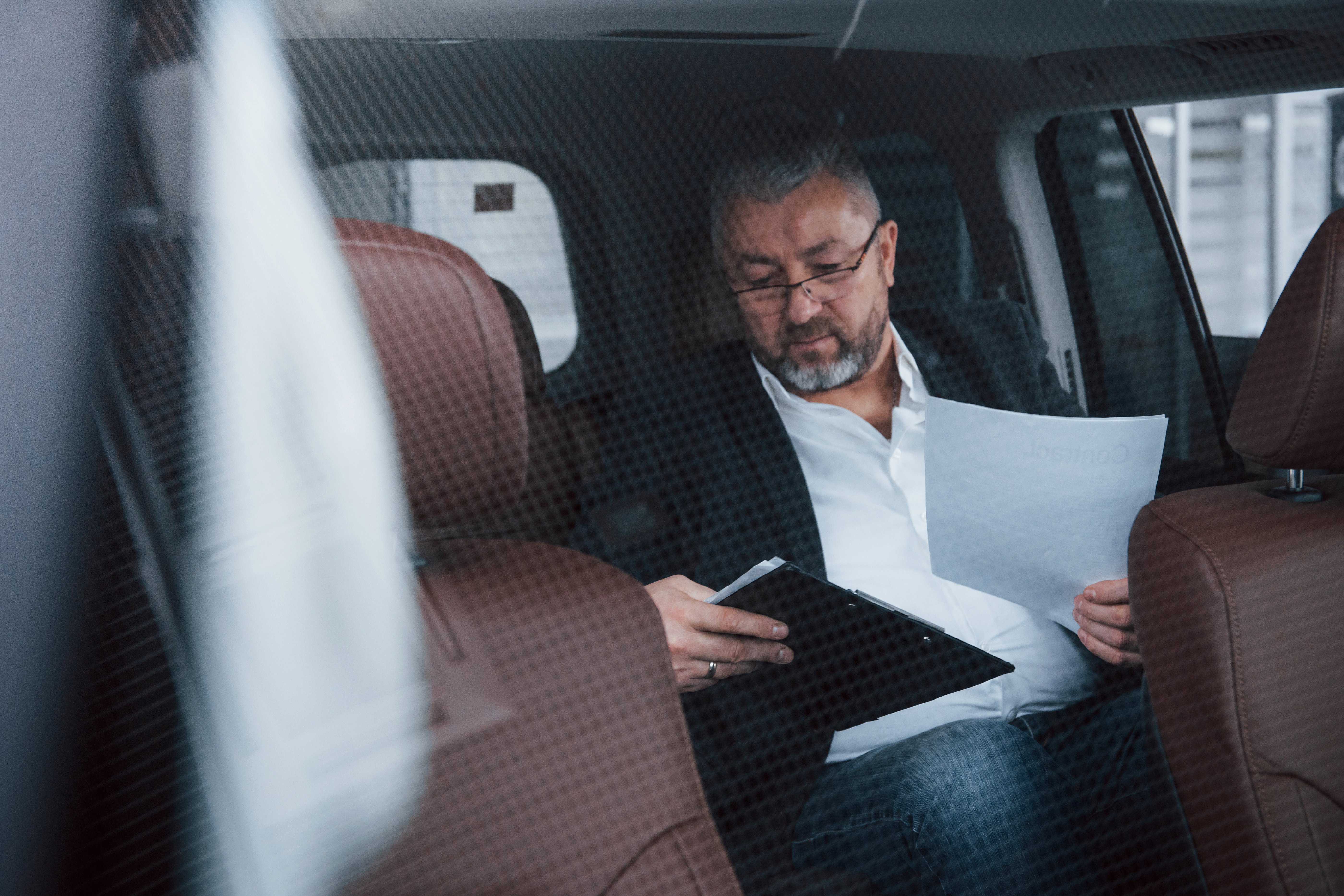  Hombre en el asiento trasero de un auto revisando documentos y tomando notas, posiblemente preparando detalles financieros o de gastos.