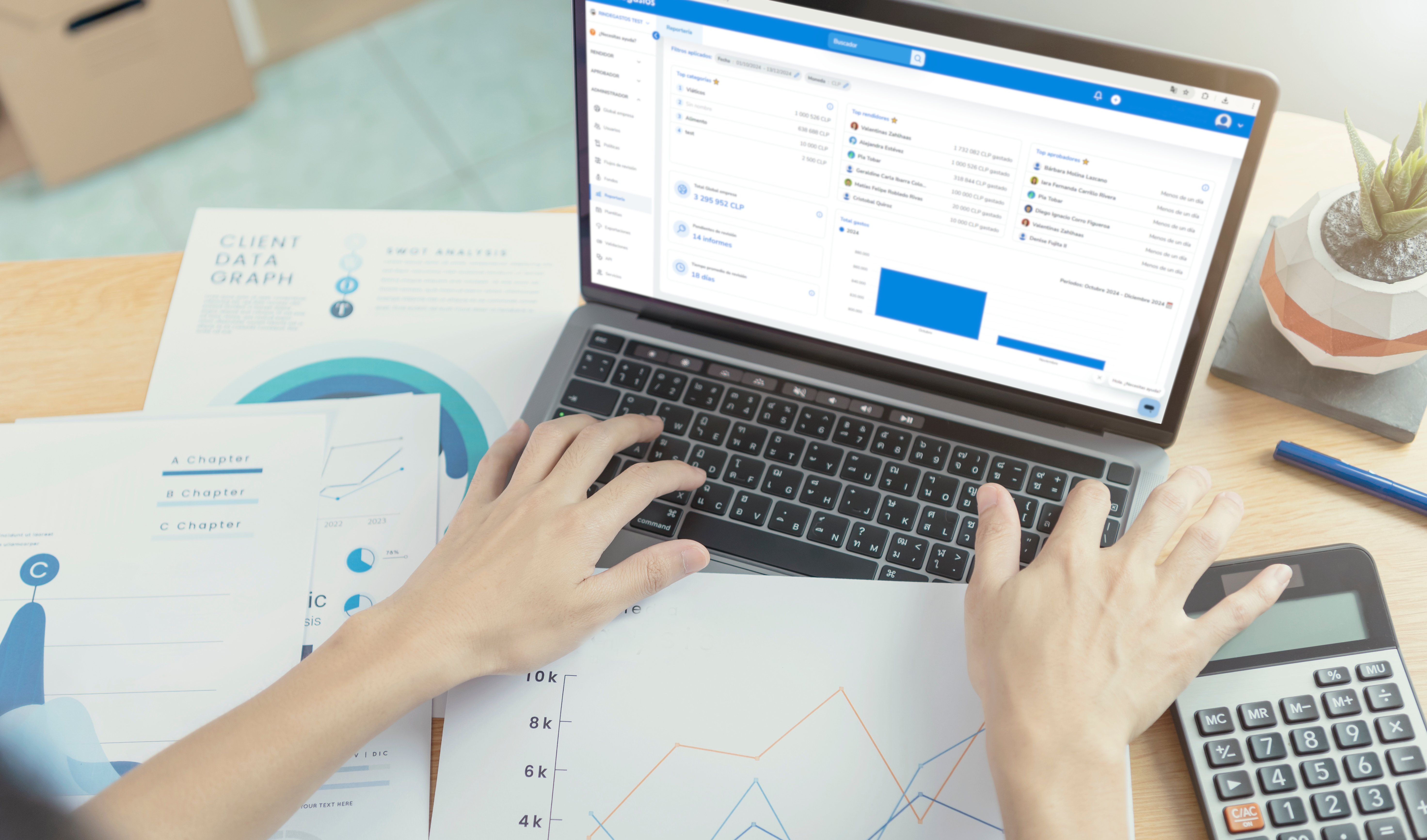 Vista superior de una persona analizando gráficos y reportes financieros en una laptop, con documentos y una calculadora en la mesa.