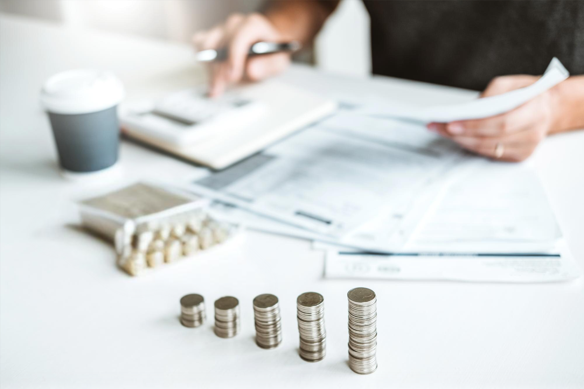 Filas de monedas apiladas en una mesa con documentos y una calculadora en segundo plano, representando la administración de finanzas y control de gastos.