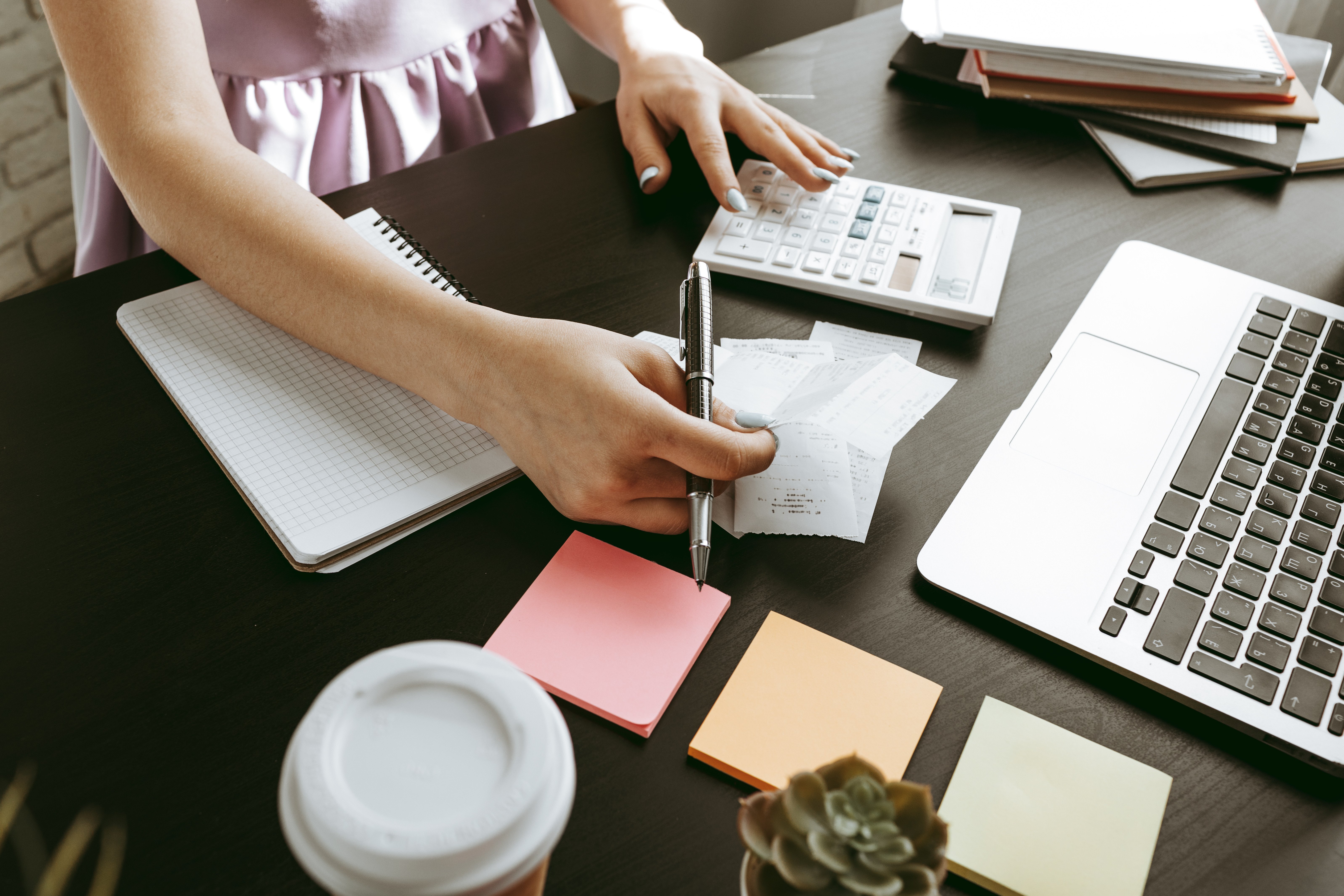 Persona organizando recibos y utilizando calculadora, acompañada de notas adhesivas y una laptop en un escritorio, representando planificación financiera.