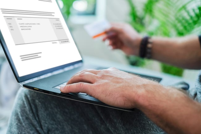 Persona gestionando un gasto y comprobante en su computadora portátil, mientras sostiene una tarjeta en la mano.