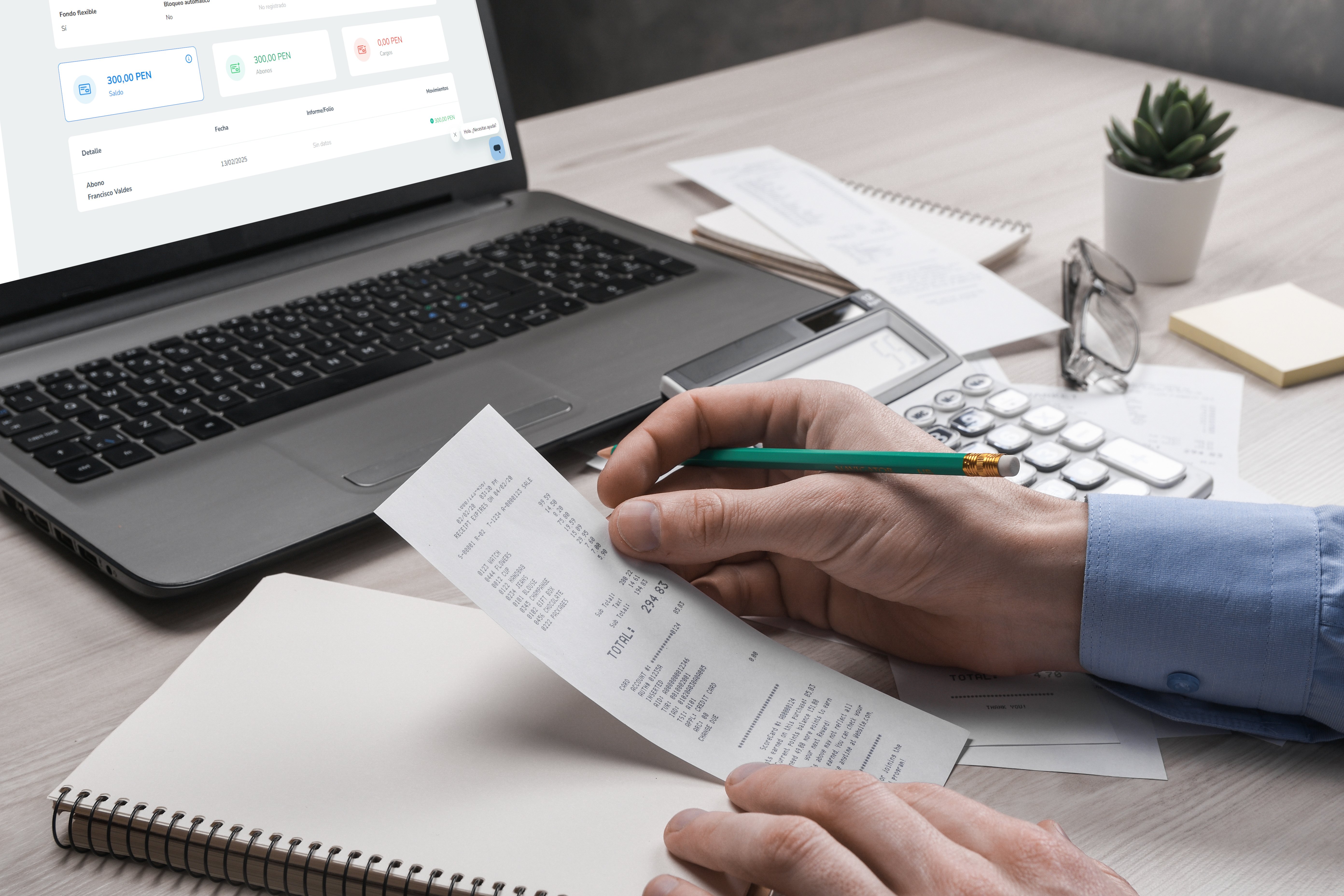 Persona sosteniendo un recibo y revisándolo mientras utiliza un lápiz para anotar en una libreta. En la mesa se encuentran una laptop con la interfaz de software de gestión de gastos visible, una calculadora, gafas y notas adhesivas.