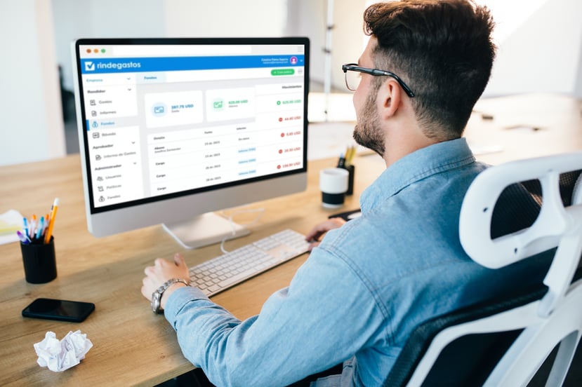 Persona trabajando frente a una computadora con la plataforma de Rindegastos abierta, mostrando el balance de fondos y movimientos recientes.